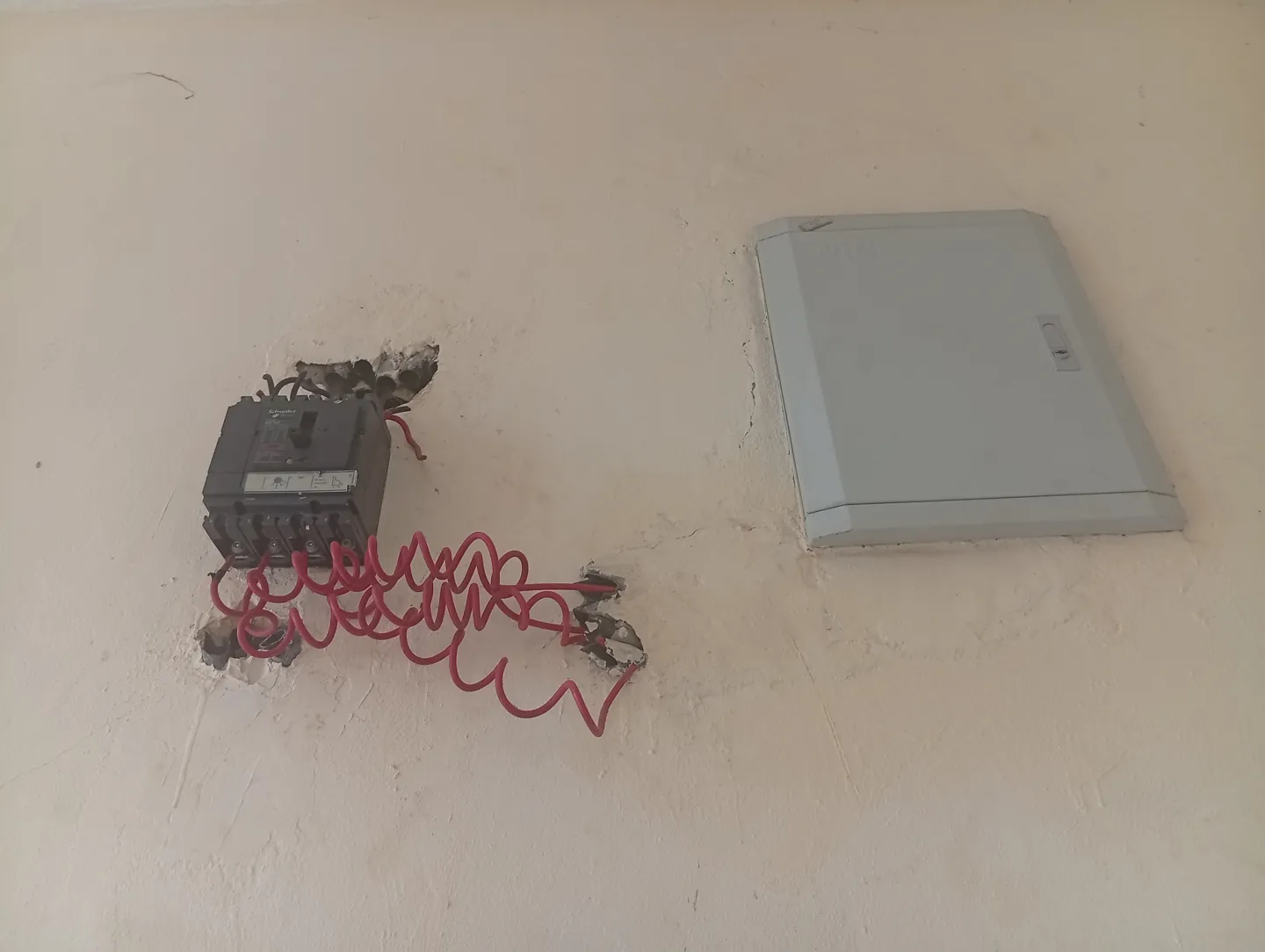 Nyitott elektromos egység vörös vezetékekkel, mellette zárt elosztódoboz a falon.
